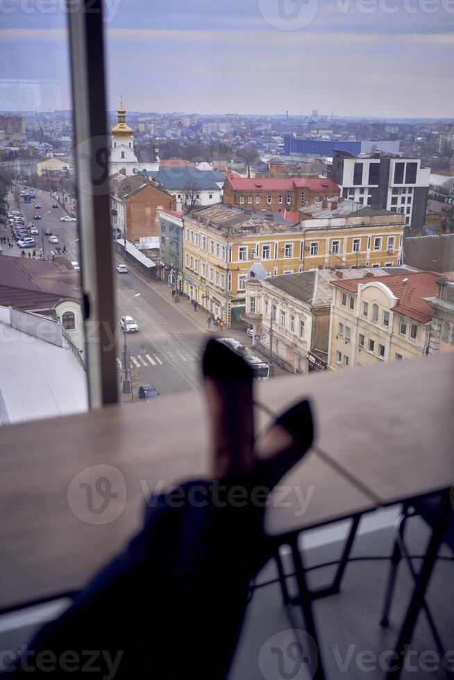 pessoa sentado dentro frente do janela com Alto salto, Preto calça e perna cruzado. paisagem urbana fora. moderno interior com neutro tons. foto