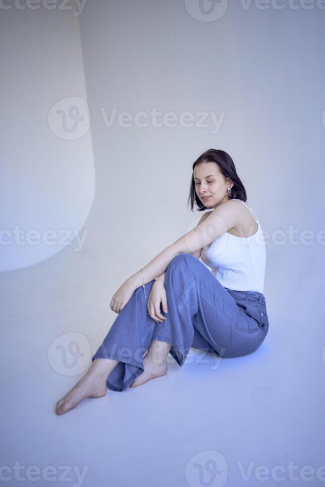 jovem Adolescência menina senta em uma branco ciclorama dentro a estúdio foto