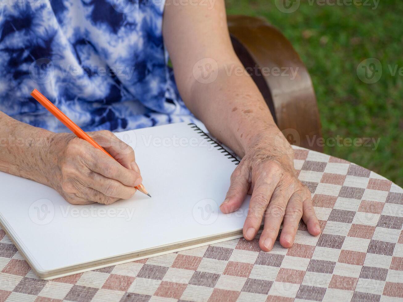 mãos do uma Senior mulher escrevendo uma livro enquanto sentado em uma cadeira dentro a jardim. fechar-se foto com cópia de espaço para texto. conceito do envelhecido pessoas e cuidados de saúde