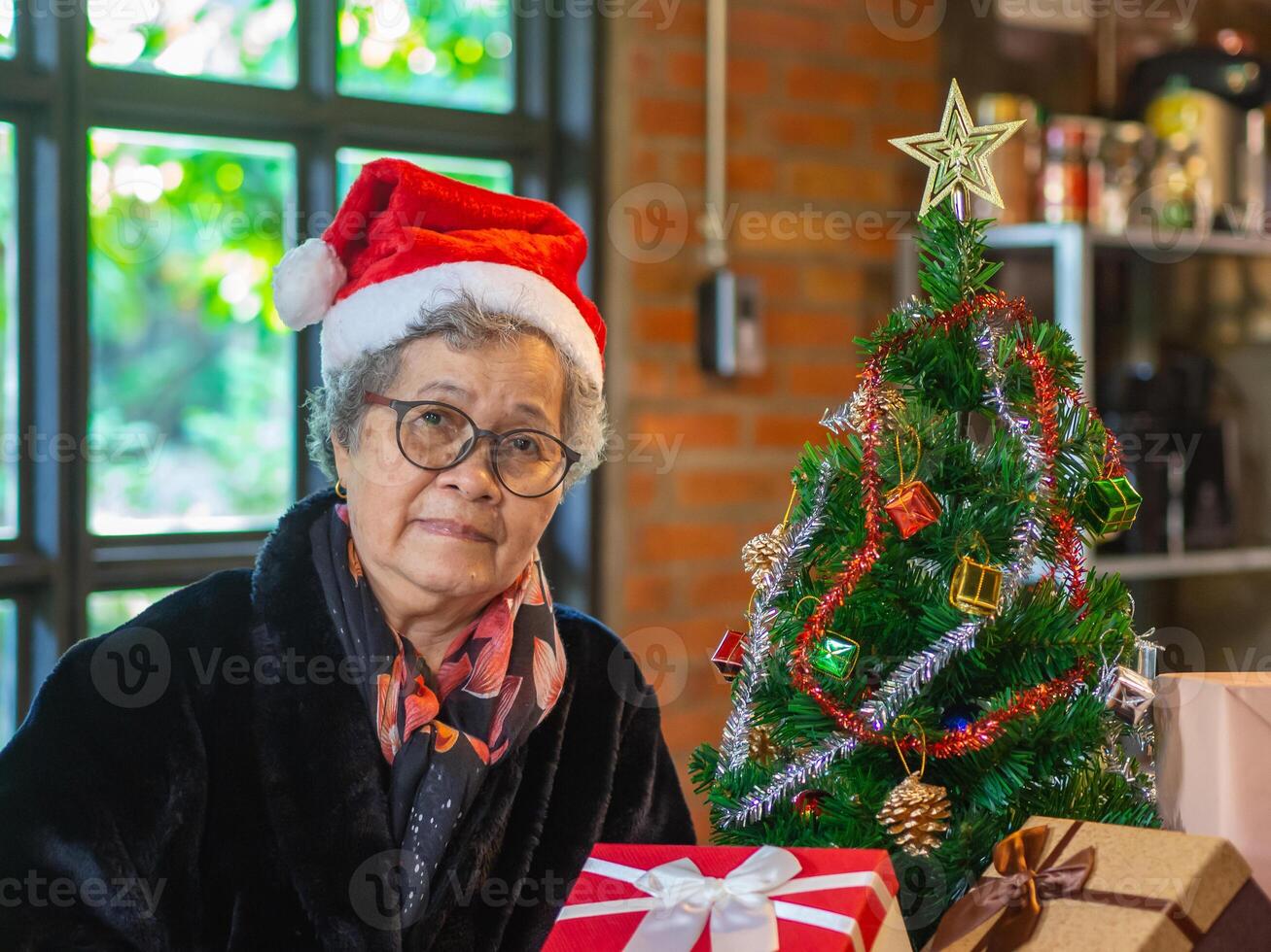 Senior ásia mulher segurando uma presente caixa e sentado perto uma Natal árvore às lar. conceito do envelhecido pessoas e festival foto