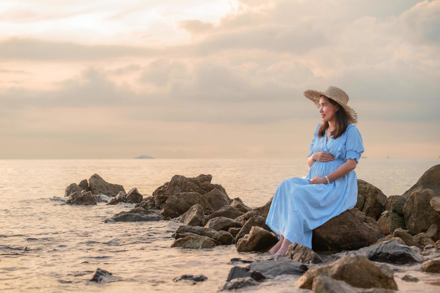 mulher grávida sentada nas rochas perto da praia de areia e do mar. foto