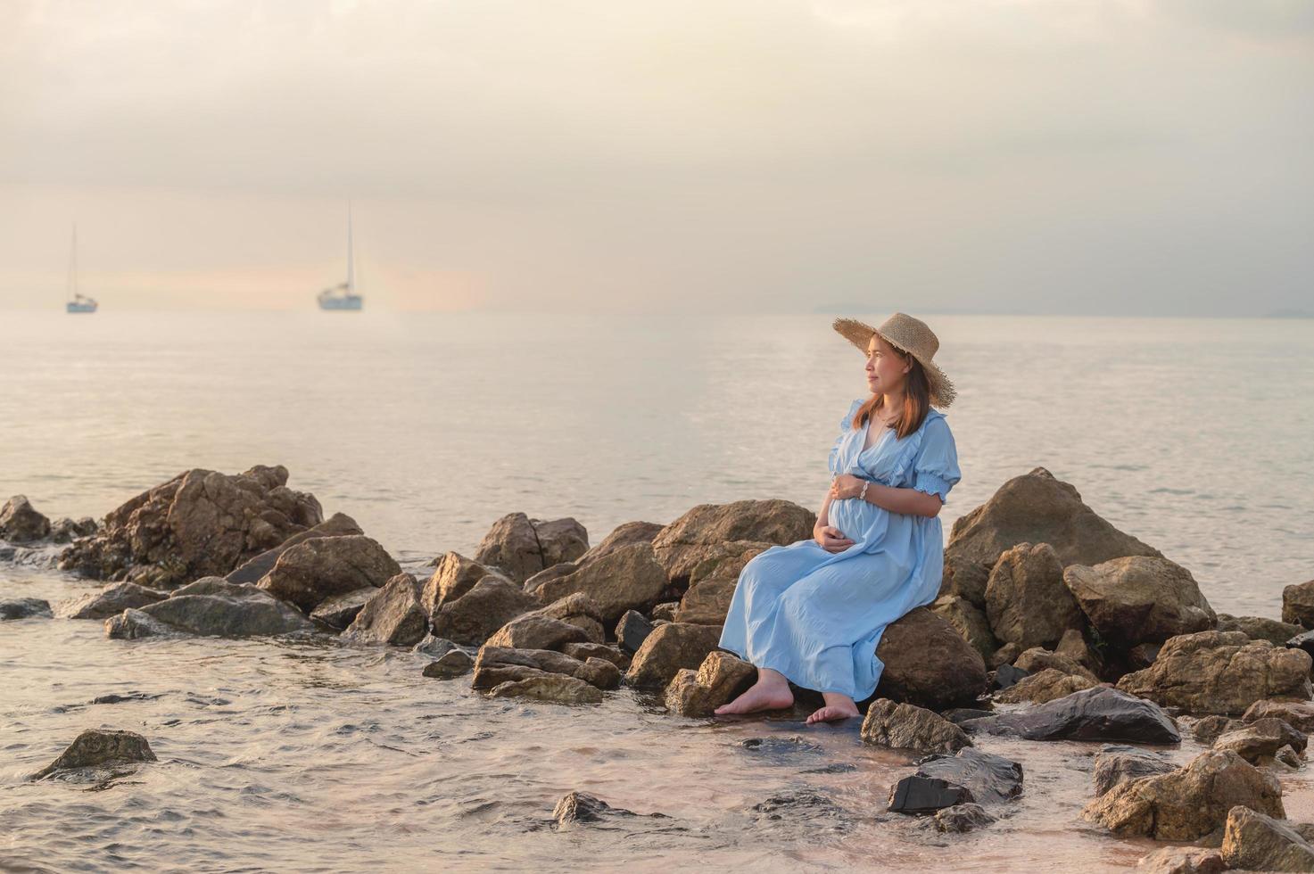 mulher grávida sentada nas rochas perto da praia de areia e do mar. foto