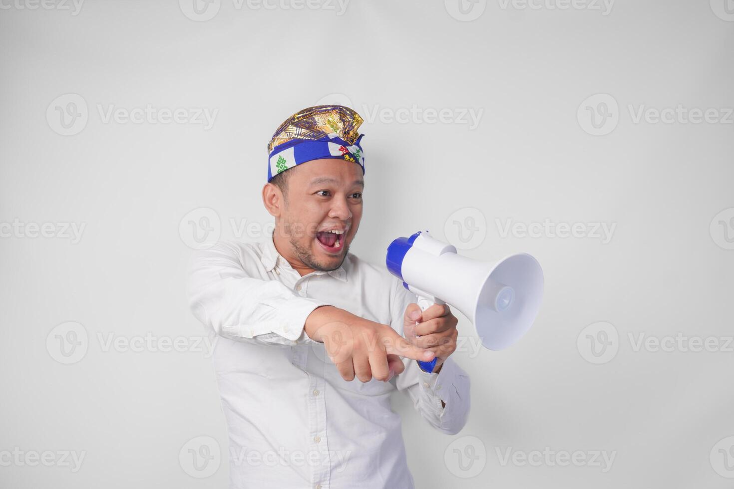 muito feliz balinesa homem dentro branco camisa e tradicional cocar gritando às megafone sentindo-me excitado, isolado de branco fundo foto