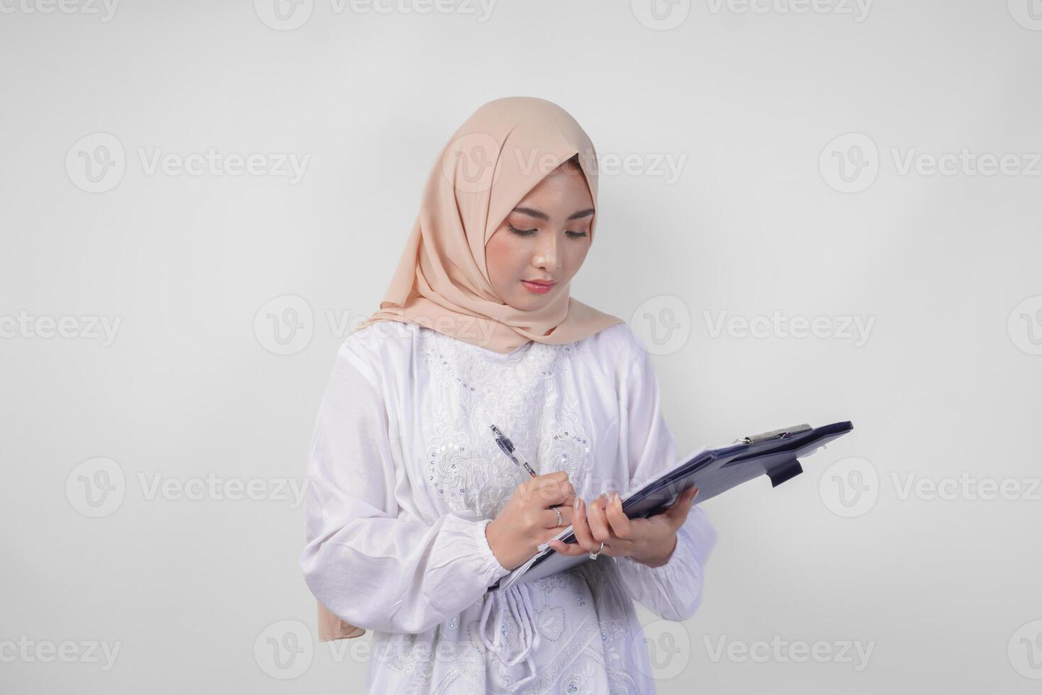 sorridente jovem ásia muçulmano mulher vestindo branco vestir e hijab segurando uma documento, isolado de branco fundo. Ramadã e eid Mubarak conceito foto