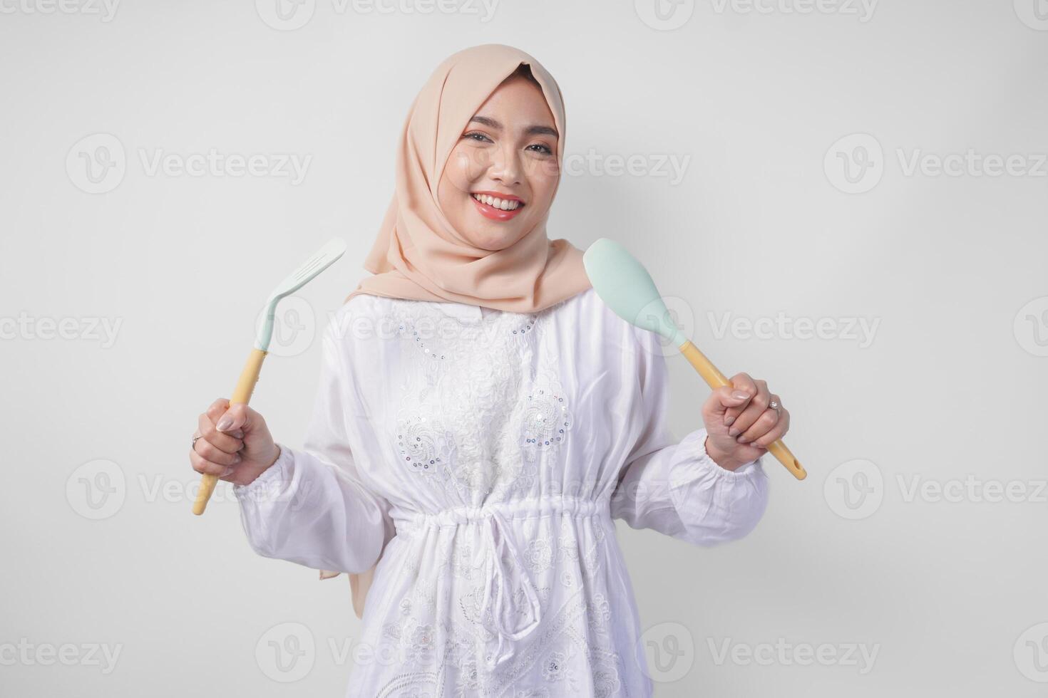 retrato do uma feliz ásia muçulmano mulher dentro véu hijab segurando espátula e cozinha cozinhando utensílios enquanto sorridente alegremente. Ramadã conceito foto