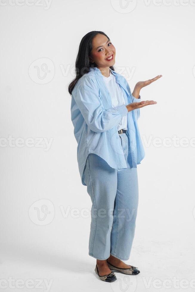 sorridente jovem ásia menina vestindo azul camisa é em pé e apontando para uma cópia de espaço ao lado dela. foto