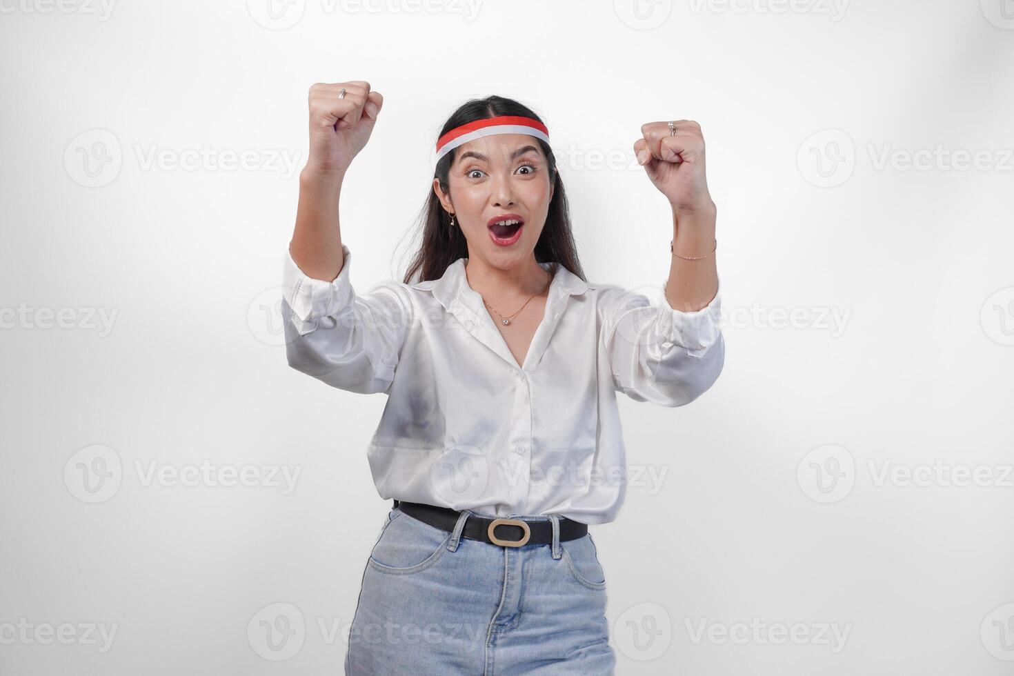 retrato do a animado jovem ásia mulher levantando punho acima gesto, ganhando e a comemorar vitória pose, vestindo bandeira arco de cabelo e branco camisa. independência dia conceito foto