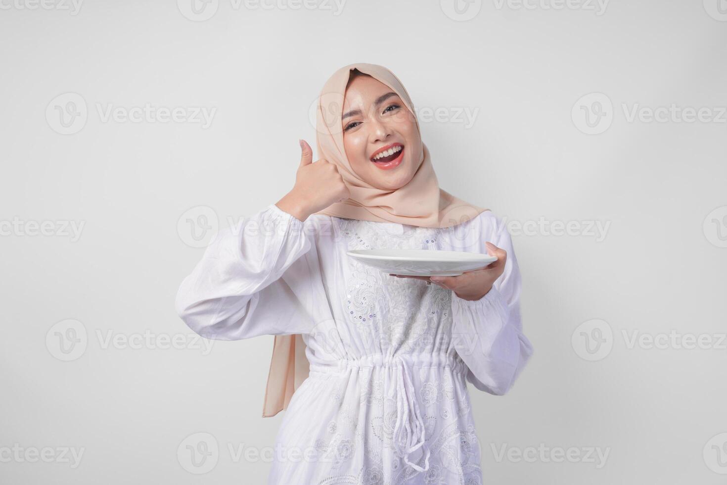 animado jovem ásia muçulmano mulher dentro hijab apresentando esvaziar branco prato cópia de espaço enquanto fazendo polegares acima gesto foto
