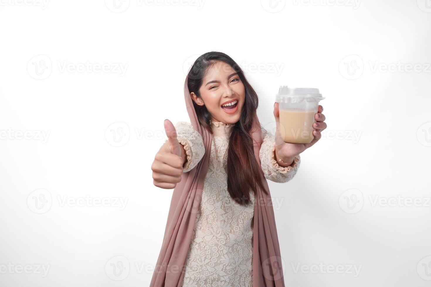 animado ásia muçulmano mulher dentro lenço de cabeça véu hijab dando polegares acima enquanto segurando café dentro uma plástico copo esperando para iftar para bebida. Ramadã conceito foto