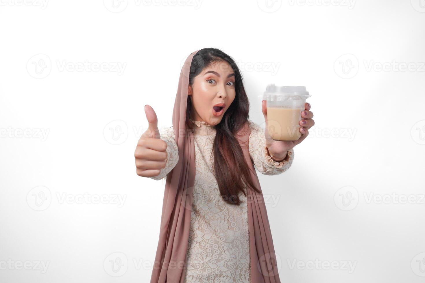 animado ásia muçulmano mulher dentro lenço de cabeça véu hijab dando polegares acima enquanto segurando café dentro uma plástico copo esperando para iftar para bebida. Ramadã conceito foto