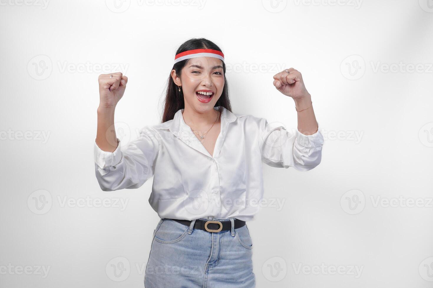 retrato do a animado jovem ásia mulher levantando punho acima gesto, ganhando e a comemorar vitória pose, vestindo bandeira arco de cabelo e branco camisa. independência dia conceito foto