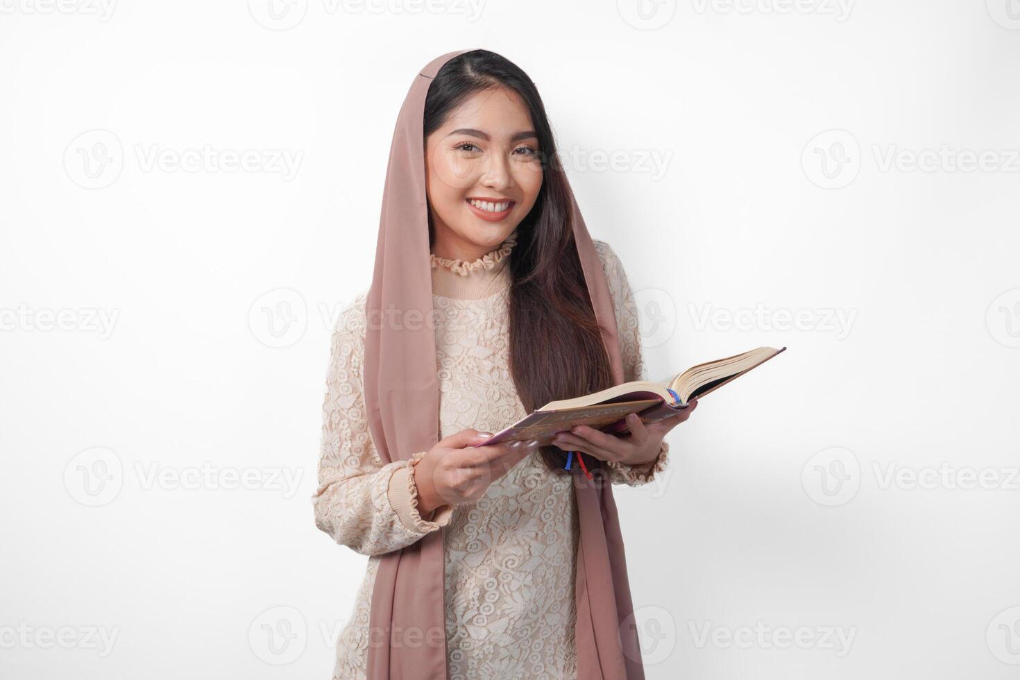 retrato do uma jovem ásia muçulmano mulher dentro véu hijab sorridente para a Câmera enquanto segurando al alcorão. Ramadã e eid Mubarak conceito foto