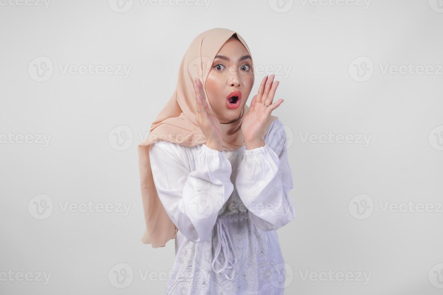 lindo jovem ásia muçulmano mulher dentro branco vestir e hijab gritando ou anunciando notícias, emocionante evento com mãos em boca, isolado em branco fundo foto