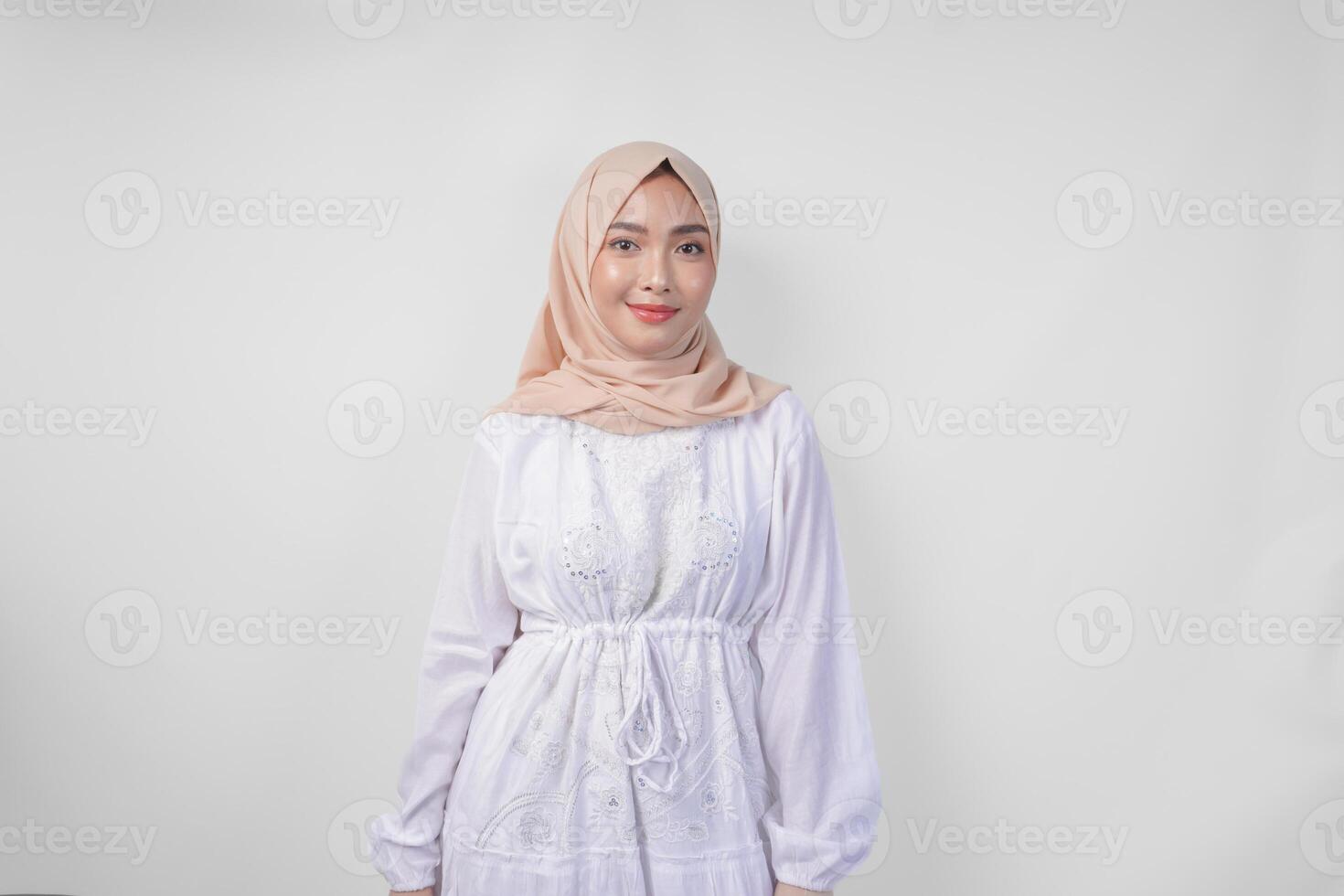 atraente ásia muçulmano mulher dentro branco vestir e hijab sorridente para a Câmera enquanto em pé formalmente sobre isolado branco fundo foto