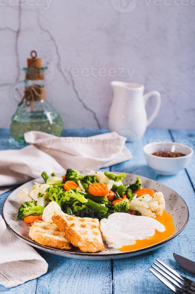 misturar do fervido vegetais, caçado ovo e waffle torrada em uma prato em a mesa vertical Visão foto