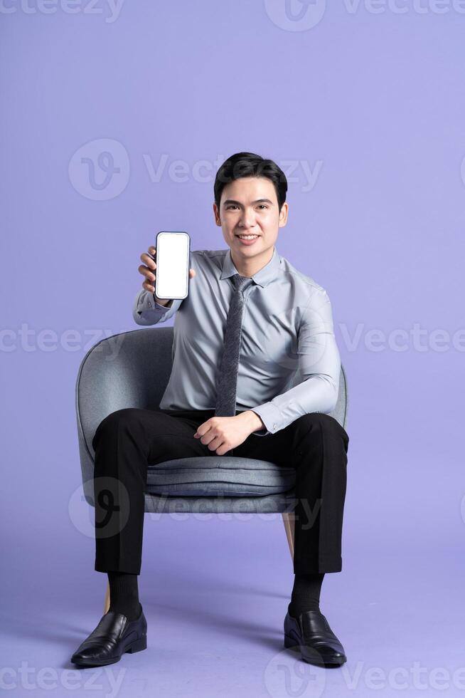 retrato do ásia o negócio homem sentado em sofá, isolado em roxa fundo foto