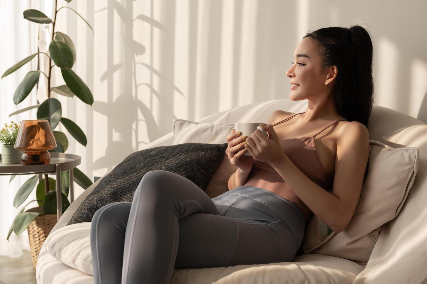 jovem ásia mulher desfrutando tendo café dentro vivo quarto às casa foto