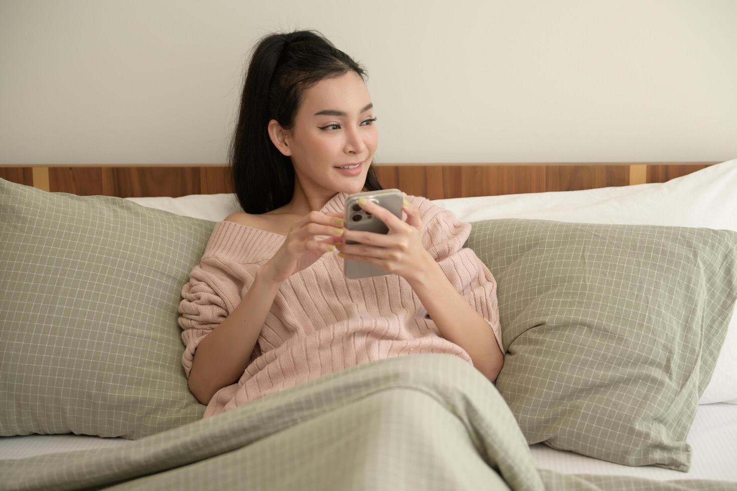 jovem ásia mulher usando inteligente telefone deitado em cama foto
