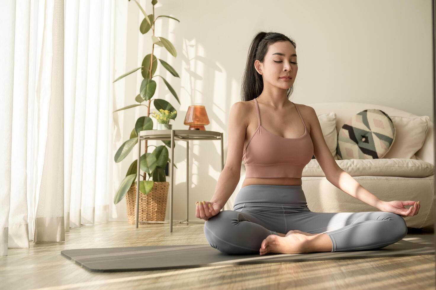 ásia mulher dentro roupa de esporte exercício e fazendo ioga dentro vivo quarto às lar, saudável estilo de vida, mental saúde conceito. foto