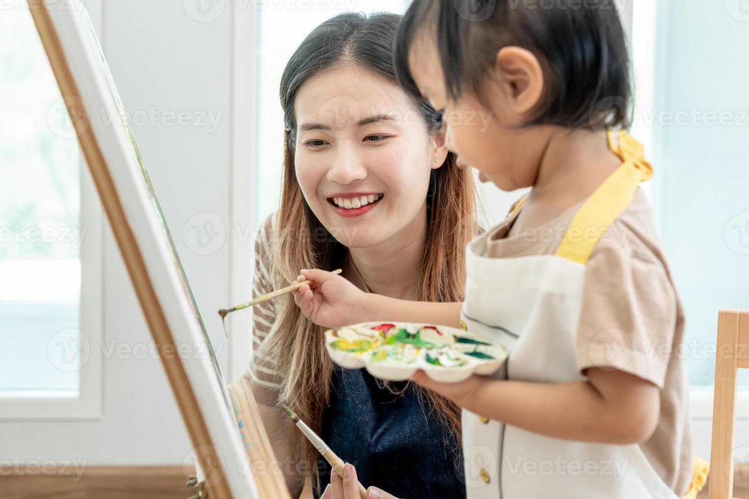 feliz Ásia mãe jogando Aprendendo pintura para pequeno garota. engraçado família é feliz e animado dentro a casa. mãe e filha tendo Diversão gastos Tempo junto. feriado, atividade foto