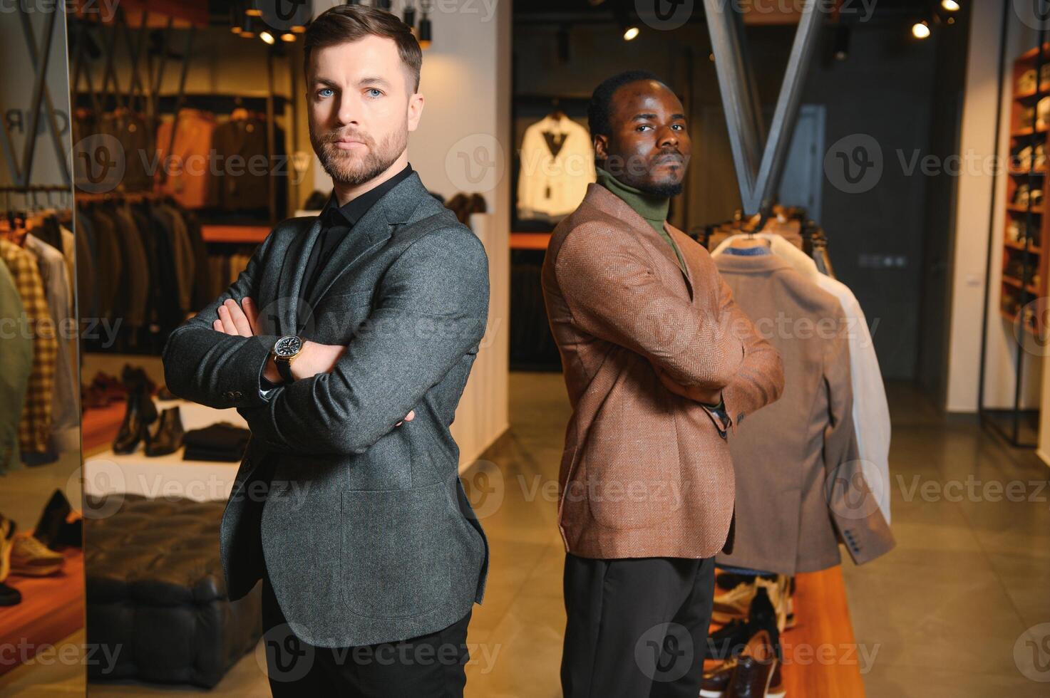dois à moda multirracial homens em pé dentro clássico ternos em pé dentro uma roupas loja foto