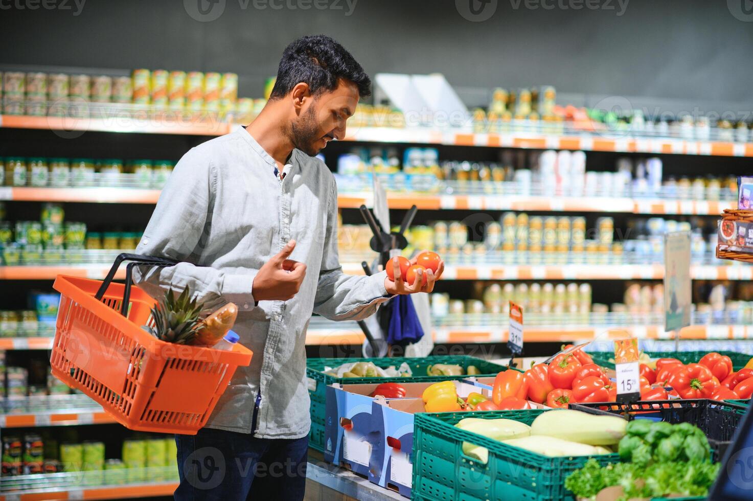 fechar-se retrato, bonito jovem homem colheita acima Sino pimentas, escolhendo amarelo e laranja legumes dentro mercearia loja foto