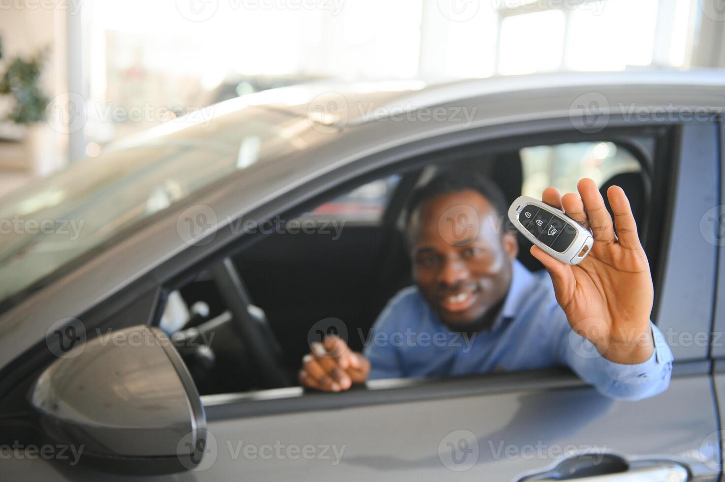 comprador de veículo africano feliz dentro de seu carro novo com chave do carro foto