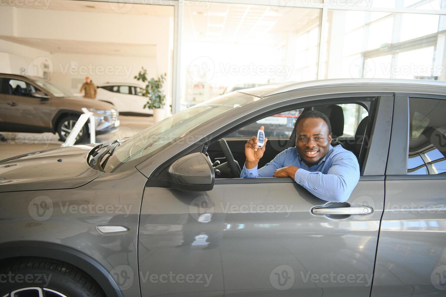 comprador de veículo africano feliz dentro de seu carro novo com chave do carro foto