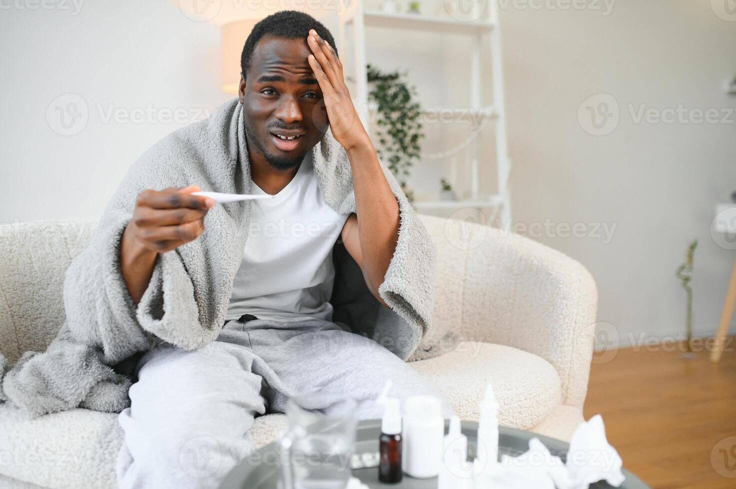 retrato do uma doente jovem africano americano homem embrulhado dentro uma cobertor em a sofá. cara com sazonal gripe ou frio sentir pouco saudável com gripe e escorrendo nariz às casa foto