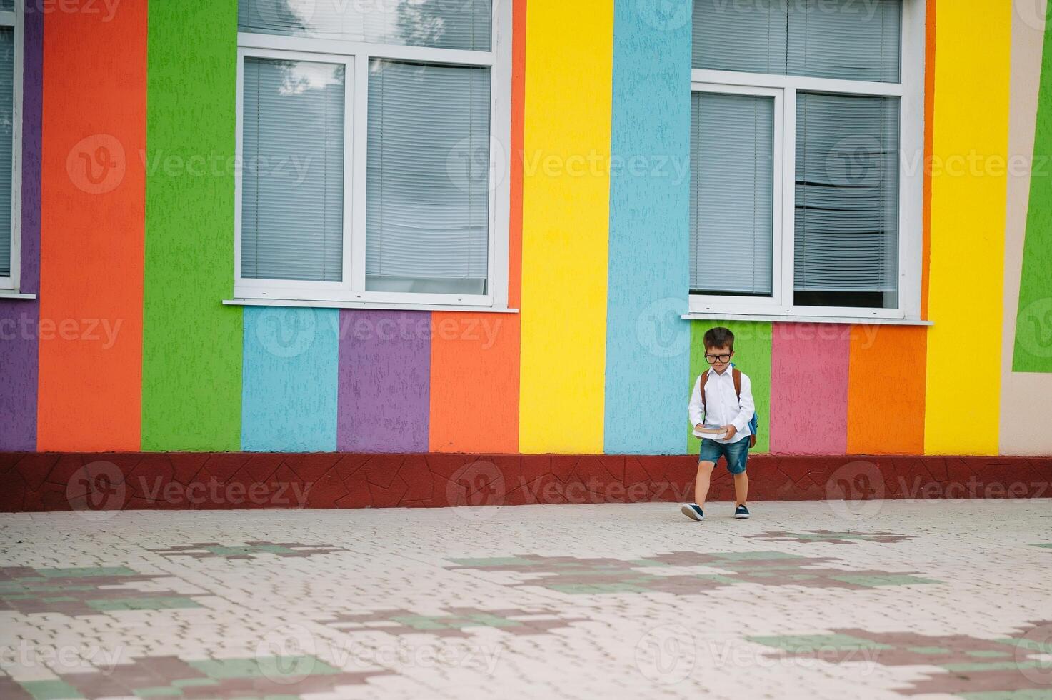 costas para escola. feliz sorridente Garoto dentro óculos é indo para escola para a primeiro tempo. criança com mochila e livro ao ar livre. começando do aulas. primeiro dia do cair. foto