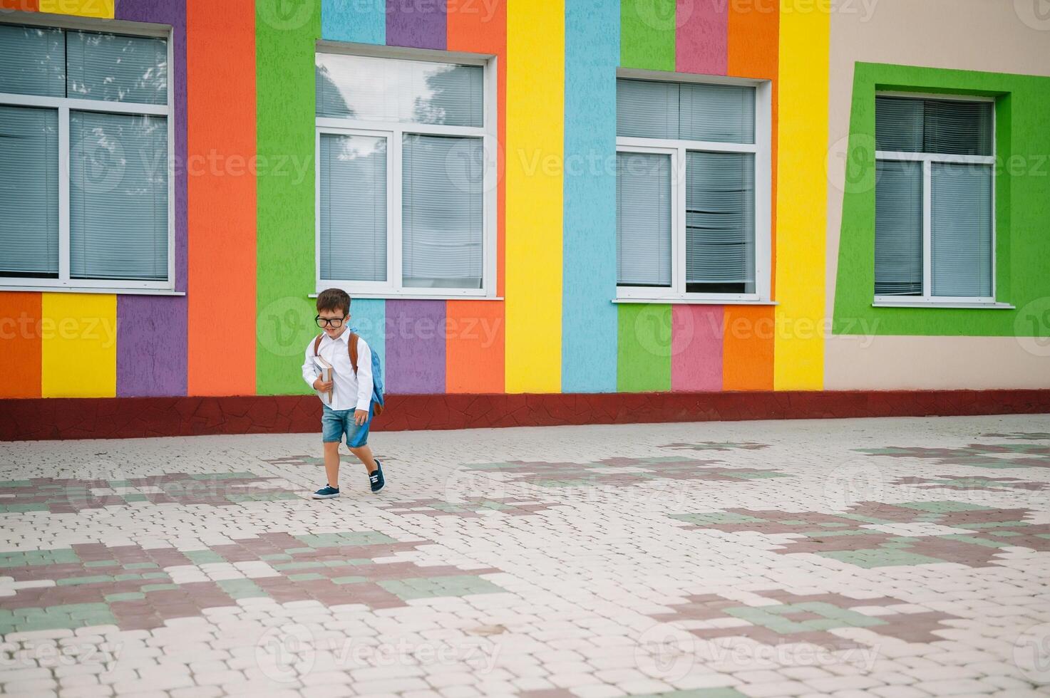 costas para escola. feliz sorridente Garoto dentro óculos é indo para escola para a primeiro tempo. criança com mochila e livro ao ar livre. começando do aulas. primeiro dia do cair. foto