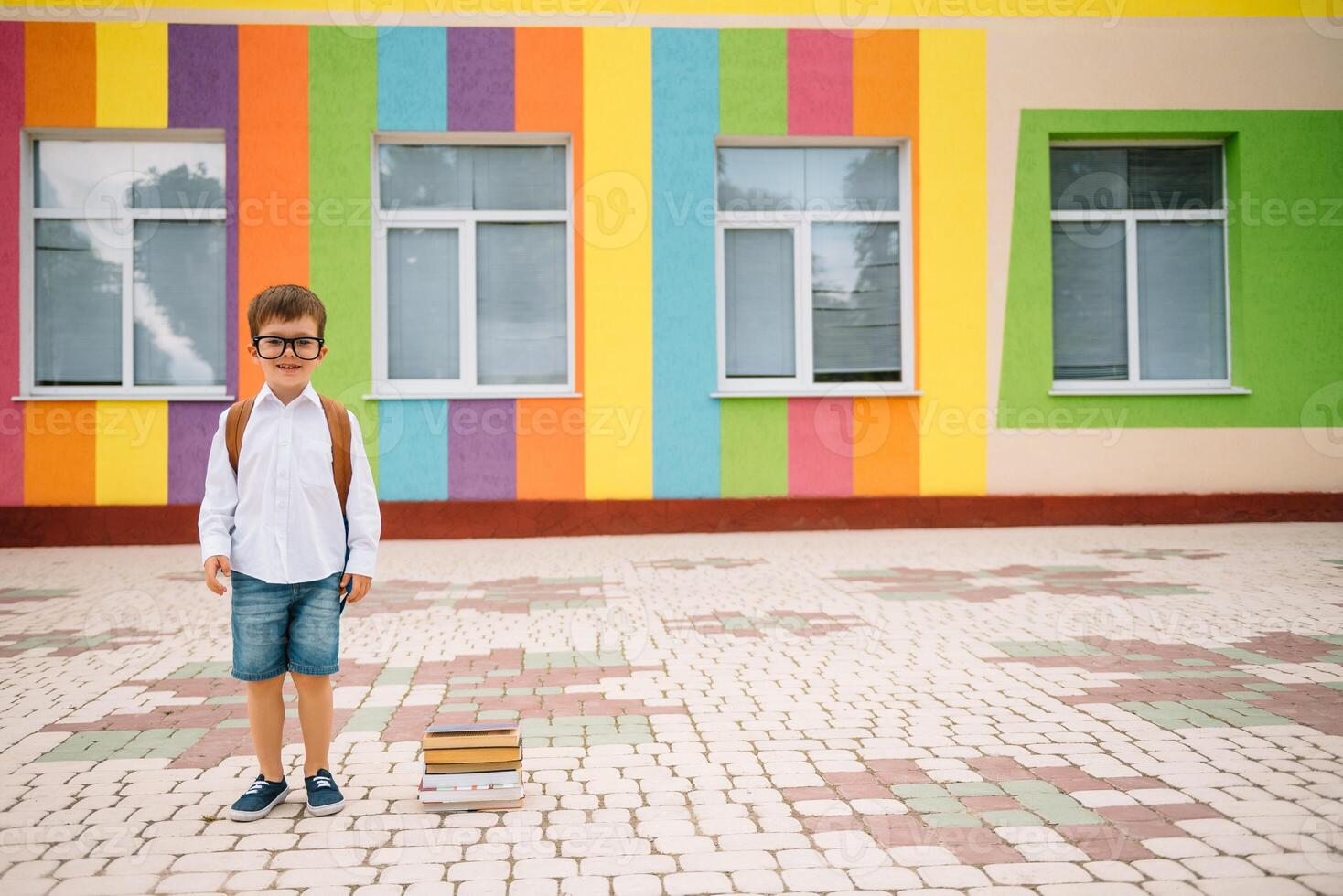 costas para escola. feliz sorridente Garoto dentro óculos é indo para escola para a primeiro tempo. criança com mochila e livro ao ar livre. começando do aulas. primeiro dia do cair. foto