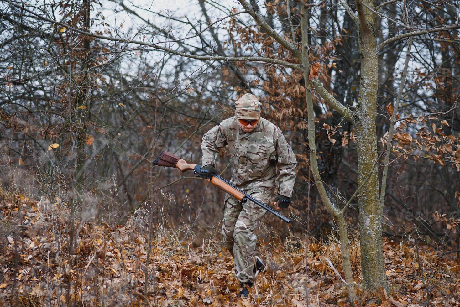 Caçando, guerra, exército e pessoas conceito - jovem soldado, guarda ou caçador com arma de fogo caminhando dentro floresta foto