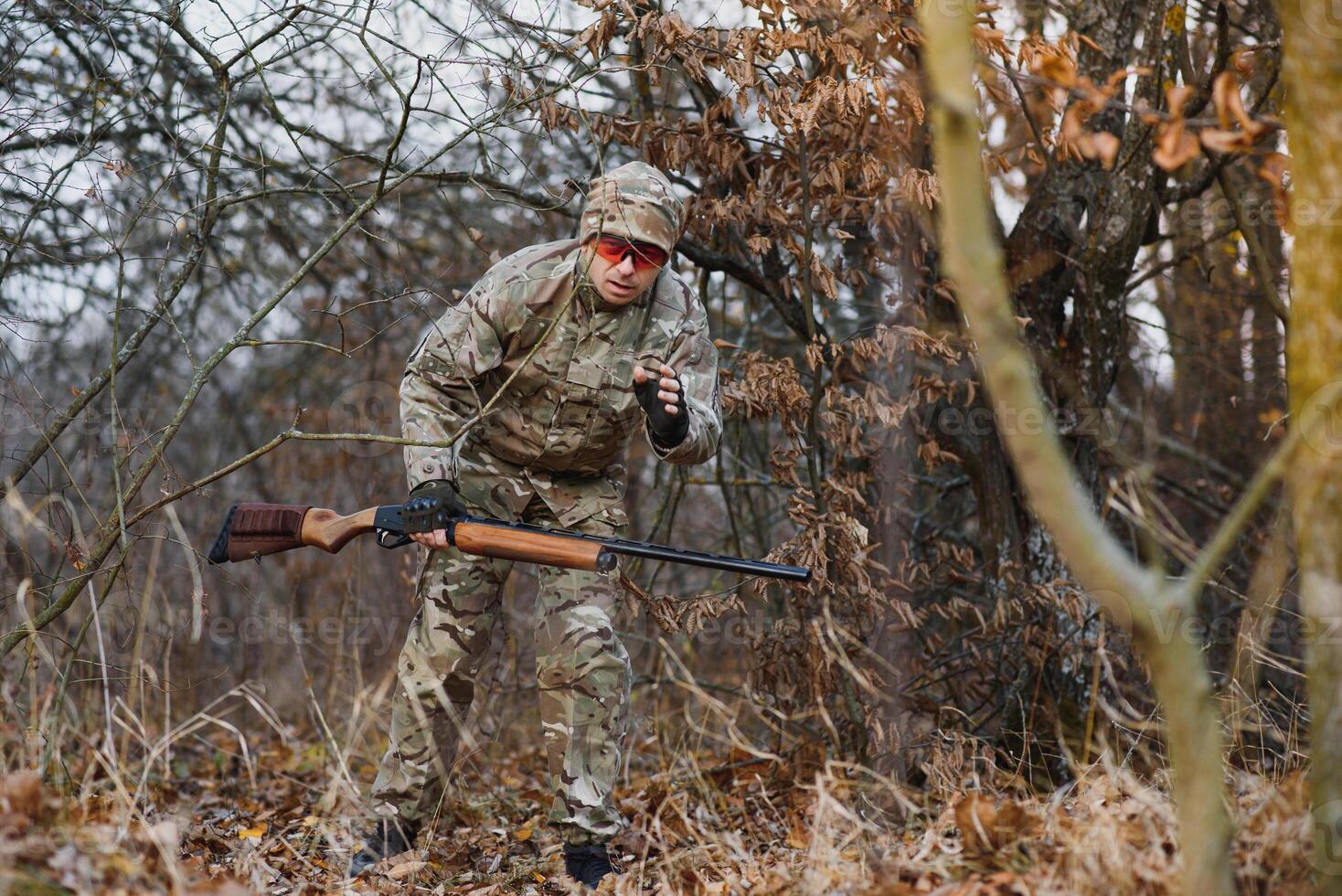 Caçando, guerra, exército e pessoas conceito - jovem soldado, guarda ou caçador com arma de fogo caminhando dentro floresta. foto