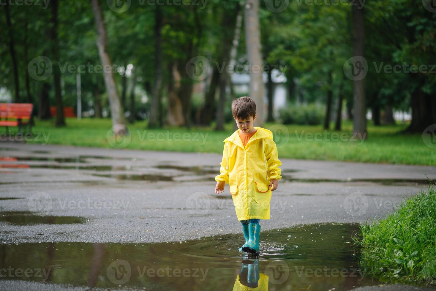 pequeno Garoto jogando dentro chuvoso verão parque. criança com guarda-chuva, à prova d'água casaco e chuteiras pulando dentro poça e lama dentro a chuva. criança caminhando dentro verão chuva ao ar livre Diversão de qualquer clima. feliz infância foto