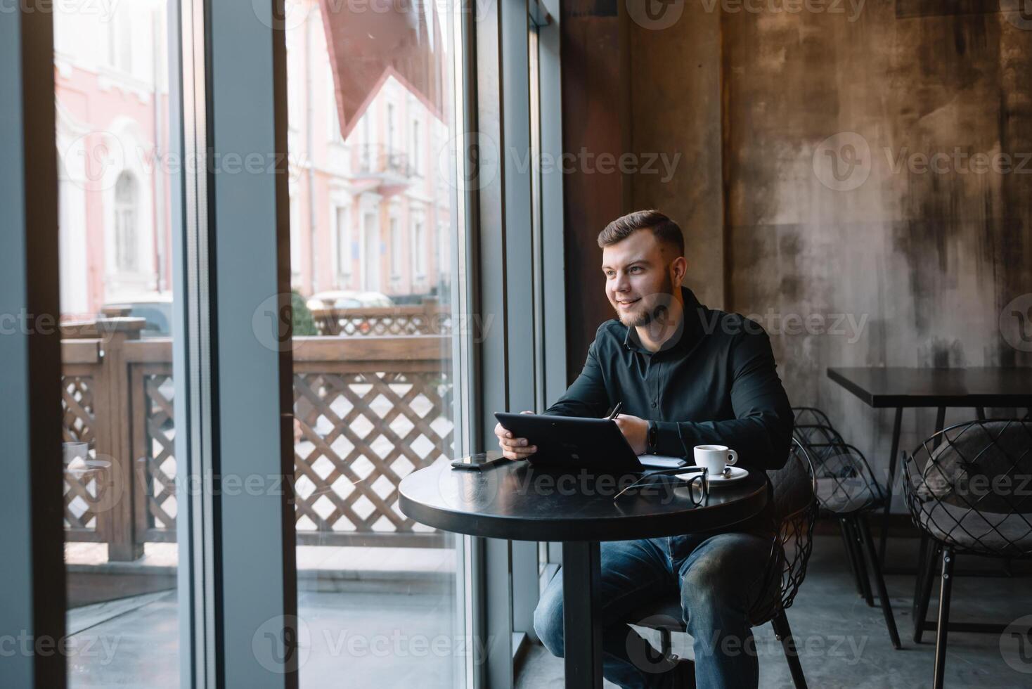 bonito homem de negocios usando uma digital tábua e bebendo café enquanto sentado dentro cafeteria dentro a cidade Centro. foto