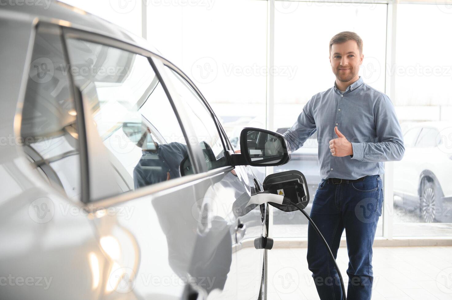 bonito o negócio homem segurando cobrando cabo para elétrico carro. caucasiano masculino carrinhos perto elétrico auto dentro concessionária foto