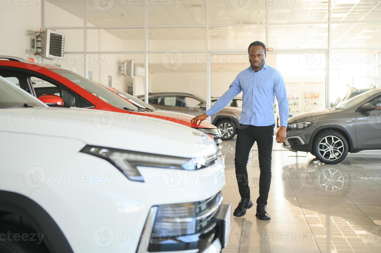 jovem afro-americano homem veio para Vejo automóveis dentro concessionária ou carros sala de exposições foto