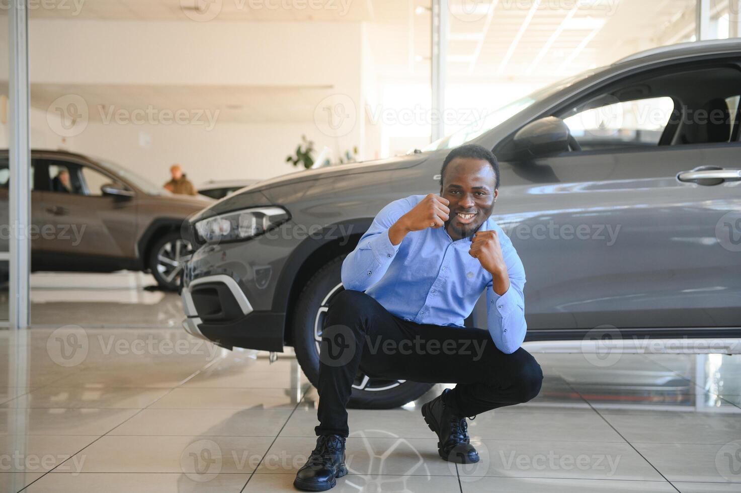 feliz carro comprador, Novo carro proprietário conceito. retrato do animado jovem africano americano cara dentro concessionária sala de exposições foto