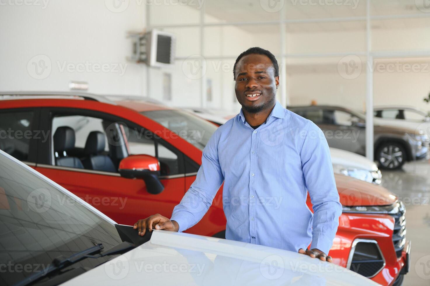 feliz carro comprador, Novo carro proprietário conceito. retrato do animado jovem africano americano cara dentro concessionária sala de exposições foto