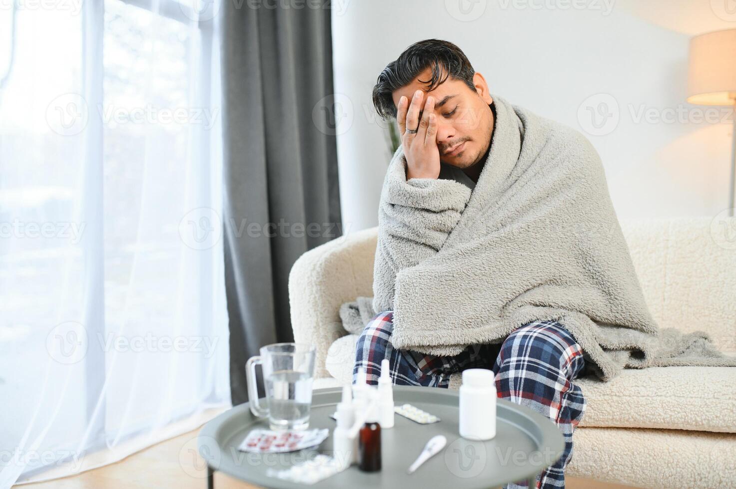 saúde, frio e pessoas conceito - doente jovem indiano homem dentro cobertor tendo dor de cabeça ou febre às casa foto