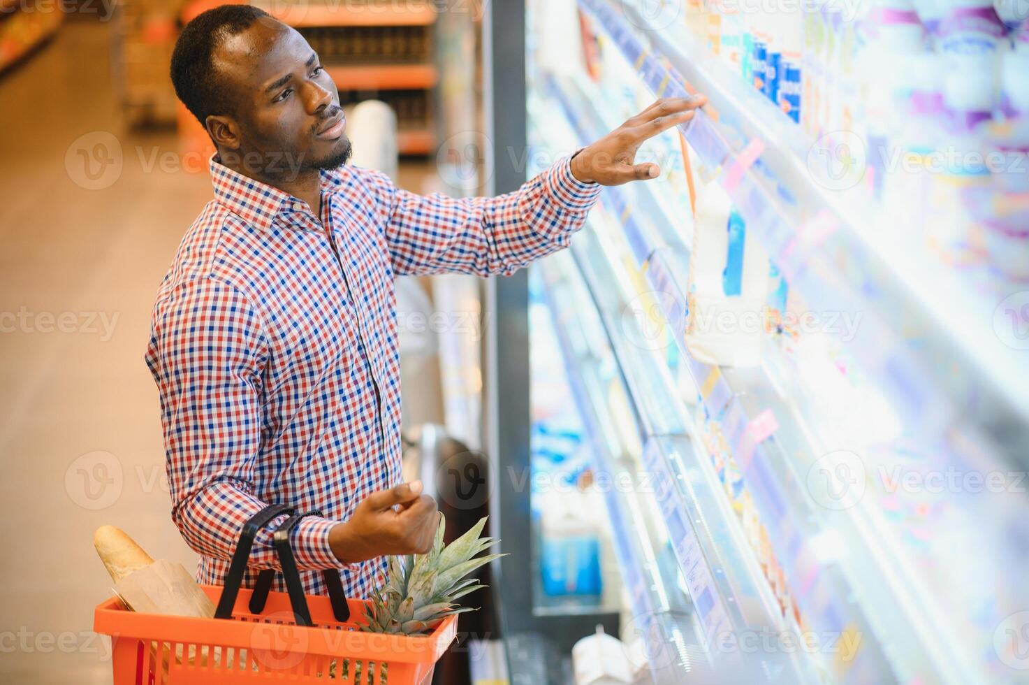 retrato do sorridente homem às supermercado. jovem africano homem com compras cesta dentro mercearia loja foto