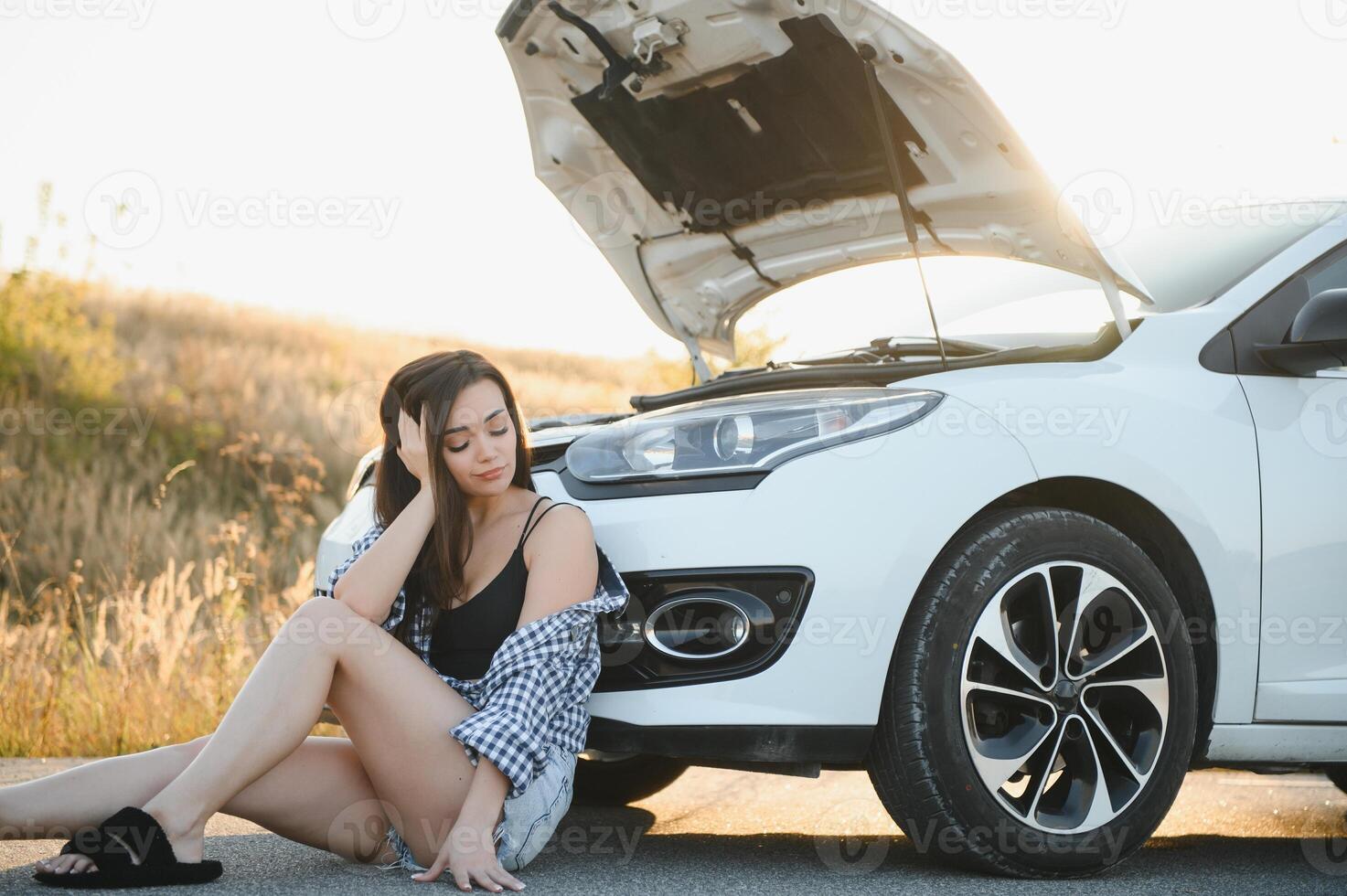 lindo jovem menina sentado às uma quebrado carro em a estrada desesperado para pegue Socorro foto