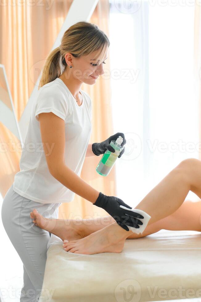 mulher mãos do uma esteticista preparando uma delgado fêmea pernas para a procedimento do açúcar cabelo remoção dentro uma profissional salão. a conceito do depilatório e pele Cuidado foto
