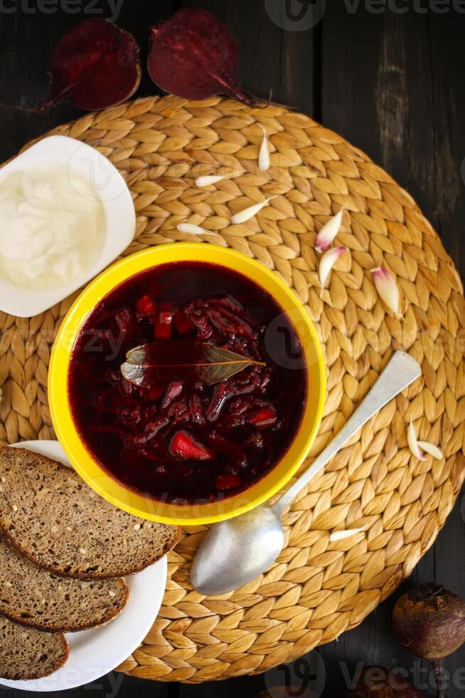 vermelho tradicional russo e ucraniano borscht ou beterraba sopa com azedo creme, alho e aromas dentro uma amarelo cerâmico copo em vime descanso de mesa fundo. foto