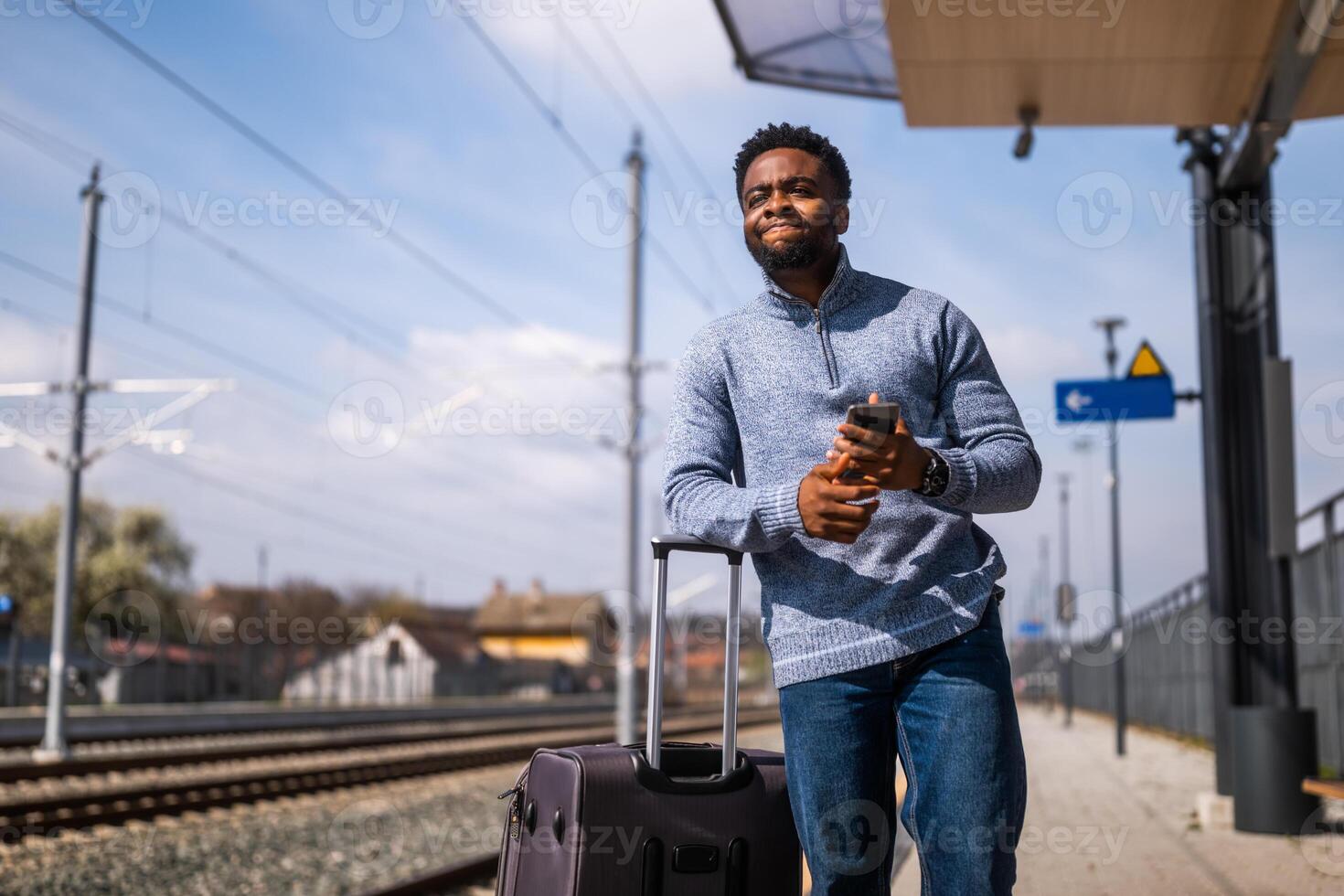 Bravo homem com uma mala de viagem e Móvel telefone em pé em uma estrada de ferro estação. foto