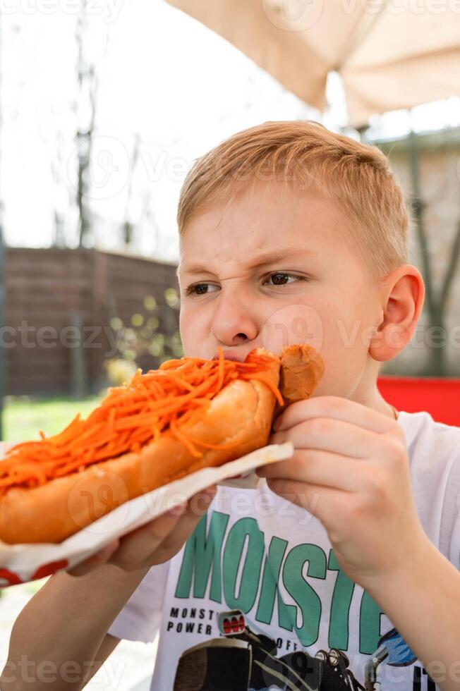 uma Garoto come uma cachorro quente às uma mesa dentro uma cafeteria dentro uma Primavera parque foto