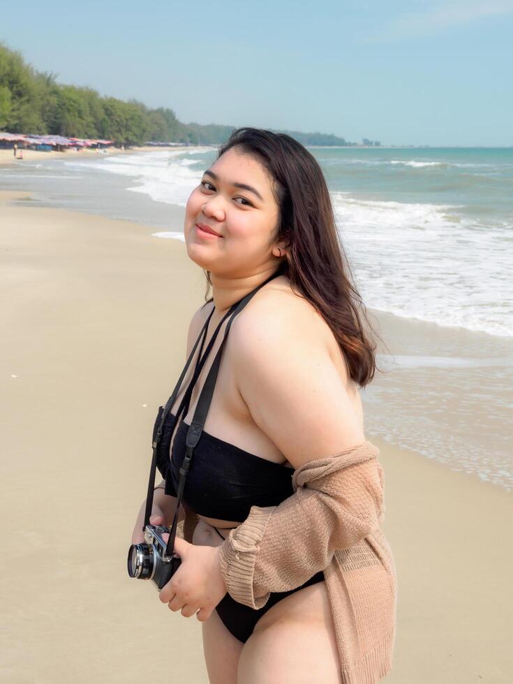 retrato jovem ásia mulher gordo gordo fofa lindo sorrir feliz Diversão apreciar relaxar bikini roupa de banho corpo sexy frente Visão mar de praia branco areia limpar \ limpo céu azul calma natureza oceano onda água viagem em feriado foto