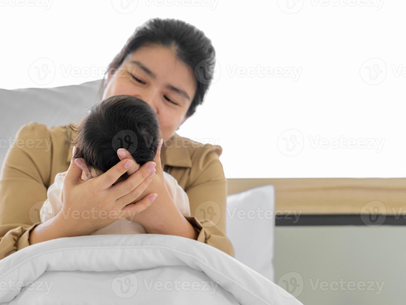 mãe segurando cabeça do dela recém-nascido bebê menina ou Garoto dentro mãos. amoroso mãe sentado dentro branco cama e segurando infantil criança. foto