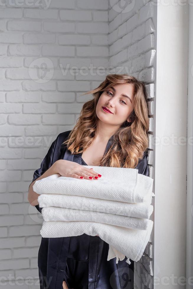 bela jovem segurando uma pilha de toalhas brancas e limpas, olhando para a câmera e sorrindo foto